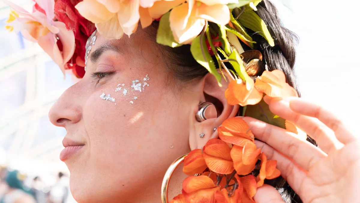 A woman at a festival in a flower crown and face glitter, wearing a silver Unplugs earplug